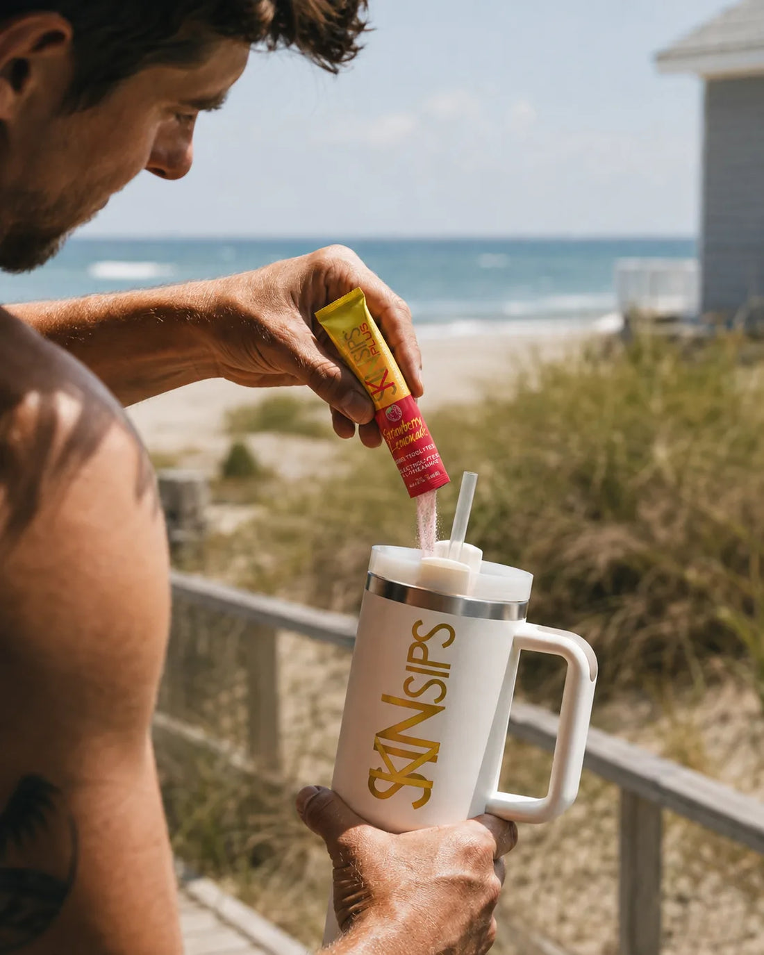 Person pouring SkinSips powder into a tumbler on a sunny beach walkway. — electrolytes and l-theanine for recovery