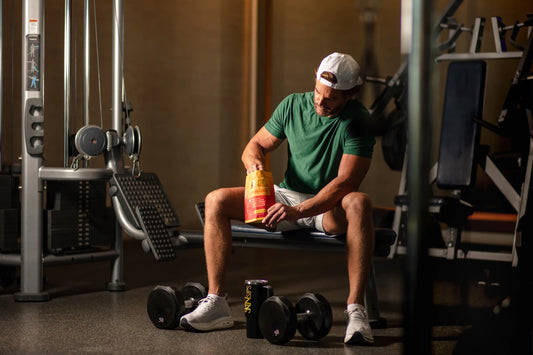 Man sitting on a gym bench holding a red and yellow drink container. — zero sugar electrolyte drink