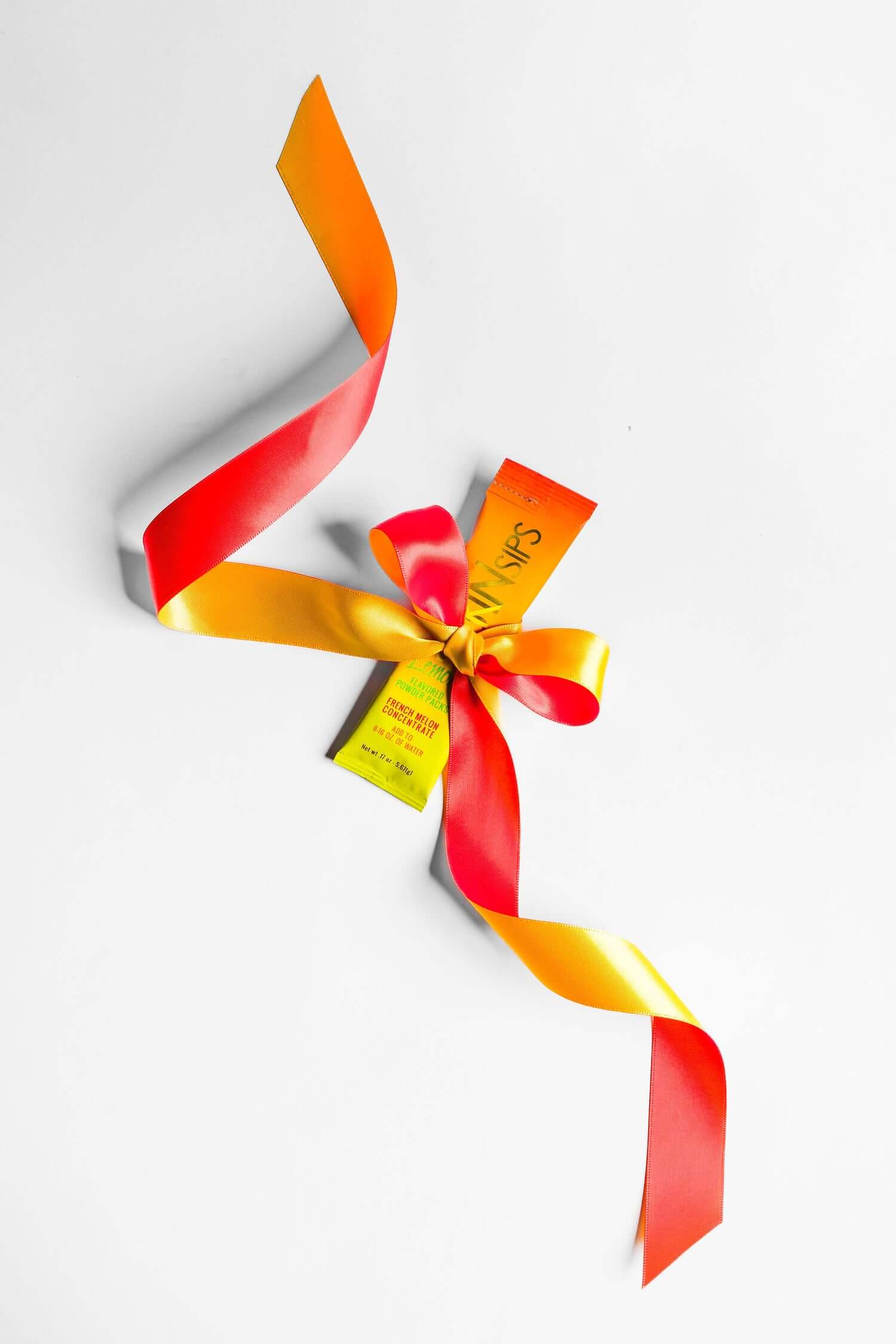 SkinSips Mango single-serve packet tied with a bright red and yellow ribbon, styled as a gift on a white background.