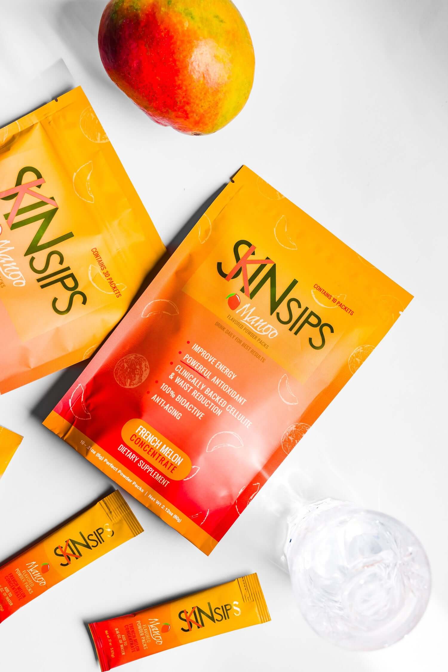 SkinSips Mango packaging displayed on a white surface alongside a fresh mango and a glass of water.